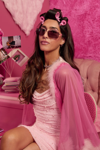 Woman wearing pink Barbie sunglasses, styled in a pink outfit with matching decor.