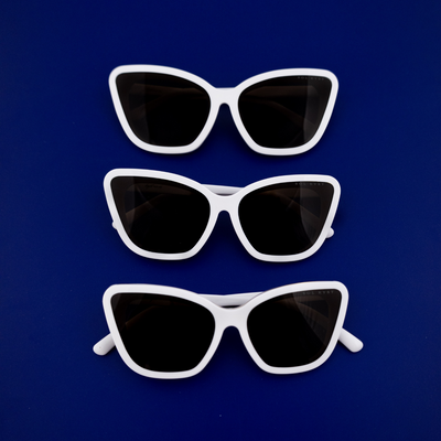 Three Sol Kyst Bridal Collection white cat-eye sunglasses arranged vertically on a vibrant blue background.