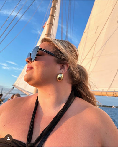 Women posing in front of boat sails, wearing black Sol Kyst cat eye sunglasses with gold accents.