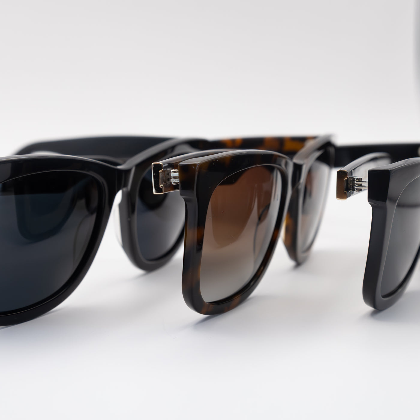 Close-up of three sunglasses in black and tortoise frames, highlighting their glossy finish and gradient lenses.