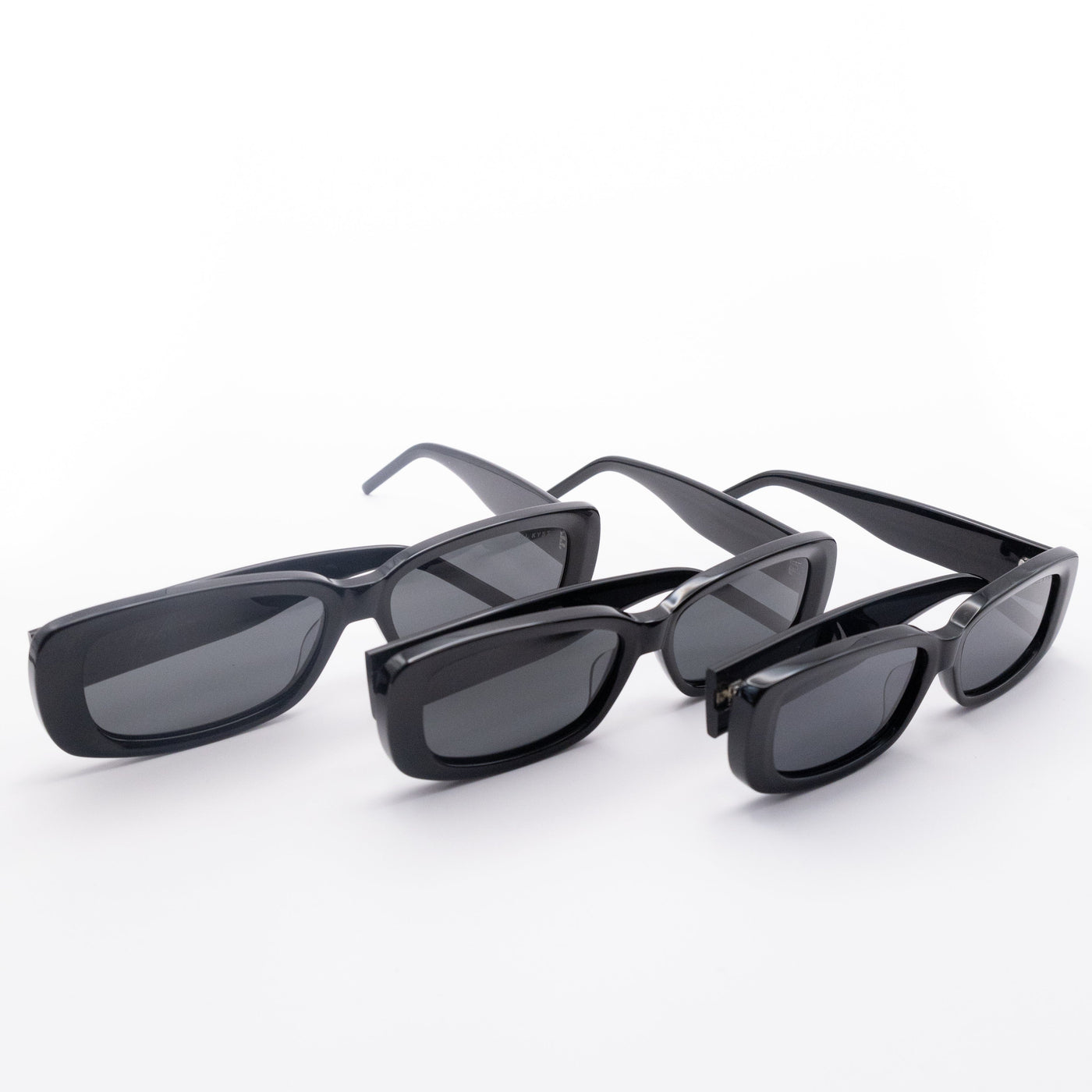 Three Sol Kyst women's rectangle sunglasses with black frames and dark tinted lenses in various sizes in a row.