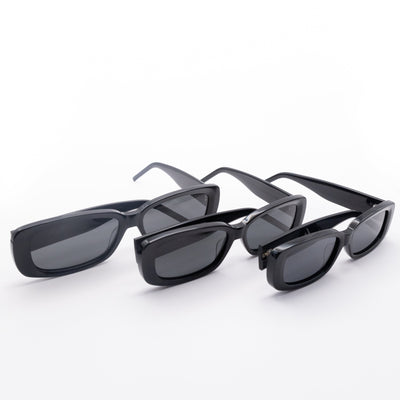 Three Sol Kyst women's rectangle sunglasses with black frames and dark tinted lenses in various sizes in a row.