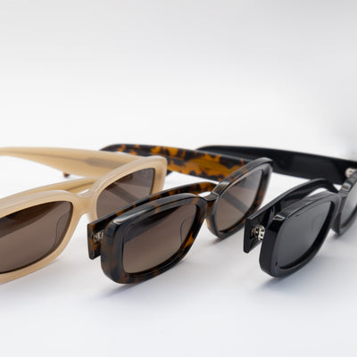 Close-up view of Sol Kyst women's rectangle sunglasses in beige, tortoise-shell, and black frames, arranged diagonally on a white background.