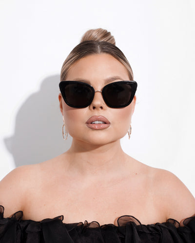 Women in black strapless dress wearing black cat eye sunglasses with dark tinted lenses on a white background.